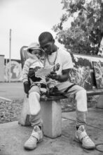 Twan reads a book to his son that they got from the Metro Library, a bus shelter that was turned into a free library with books for children. George Floyd Square, Minneapolis, Minnesota, September 26, 2020. © Patience Zalanga